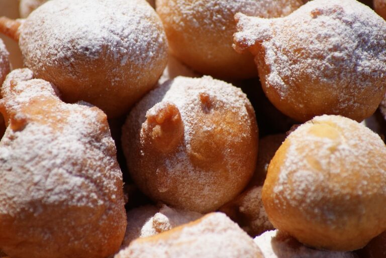 Frittelle di mele dorate su un piatto, con zucchero a velo e una fetta di mela accanto.