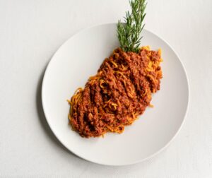 Bottiglia di vino rosso di bassa qualità accanto a un piatto di ragù in preparazione.