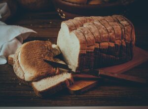 Pane fresco su un tagliere di legno, circondato da ingredienti naturali e un sacchetto di carta.