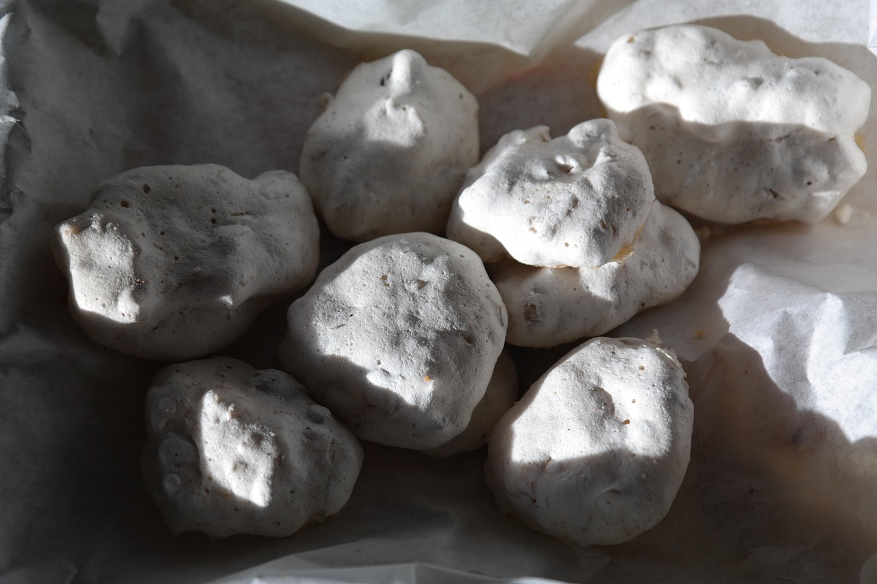 Meringhe bianche croccanti su un piatto, con forno in sottofondo e sportello socchiuso.